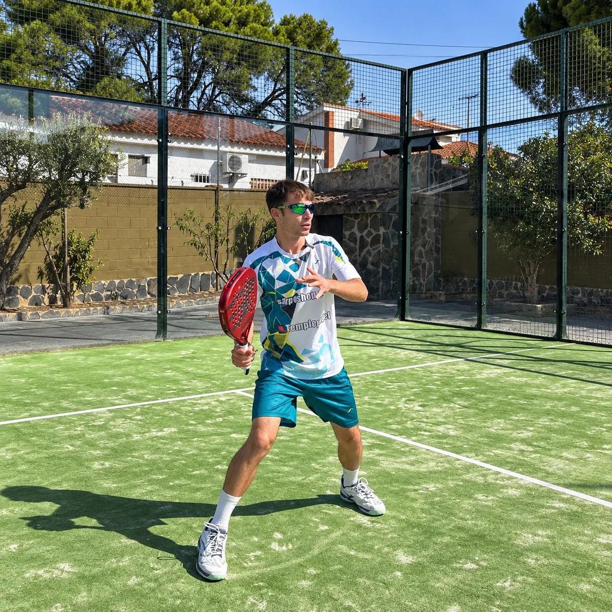 Jugador con conjunto de pádel blanco y turquesa y pala en pista exterior de césped