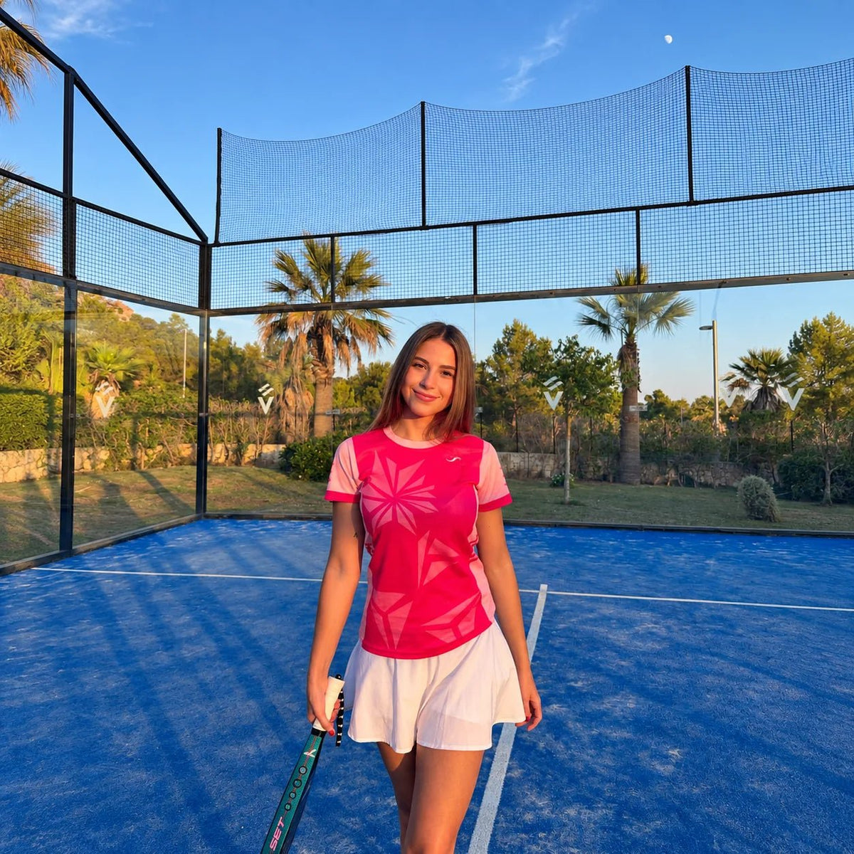 Mujer con equipación de pádel rosa fucsia y falda blanca en pista azul