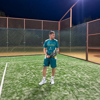 Jugador con equipación de pádel verde petróleo en posición de espera en pista de césped